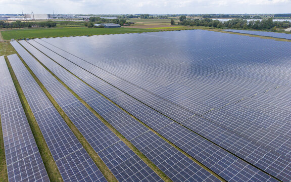 Aerial view of a large solar farm with rows of photovoltaic panels installed in a green rural landscape in Echteld, Gelderland, Netherlands.