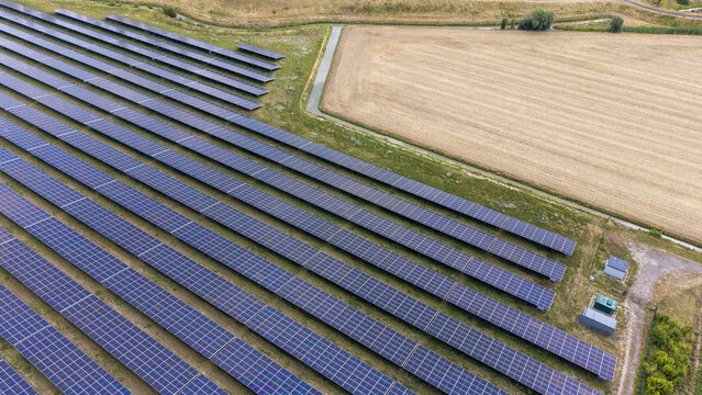 Aerial view of rows of solar panels installed in a rural field with an irrigation ditch and agricultural land in Echteld, Gelderland, Netherlands.