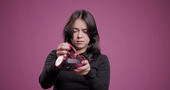 Young woman with skeptical expression examines red headphones against pink background