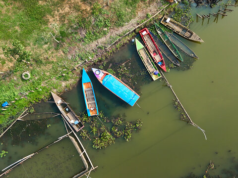 Aerial view of colorful wooden boats docked along the grassy shoreline of Rawa Pening in Waduk Rawapening, Central Java, Indonesia.