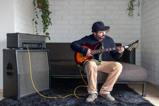 Hispanic man practicing guitar chords at home with guitar amp stack