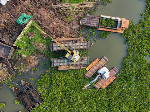 Aerial view of dredging machines operating in Rawa Pening lake to remove sediment and conserve water depth, surrounded by aquatic vegetation in Tuntang, Central Java, Indonesia.