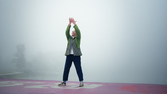 Senior Asian woman practicing tai chi in foggy outdoor nature during morning routine, active senior lifestyle and wellness concept