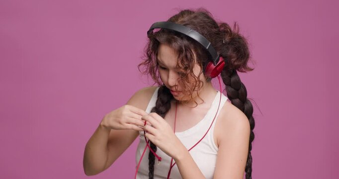 Young woman with braided hair feeling puzzled by tangled headphone wires
