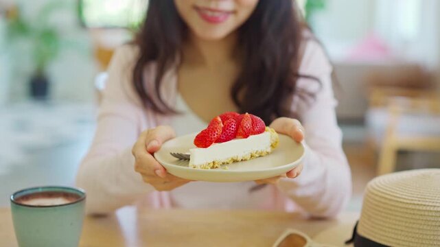 Sweet tooth and dessert indulgence concept: Happy woman enjoying strawberry cake and hot beverage on a sunny vacation day.