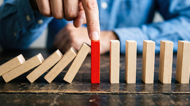 Businessman hand stopping domino effect by halting red wooden block