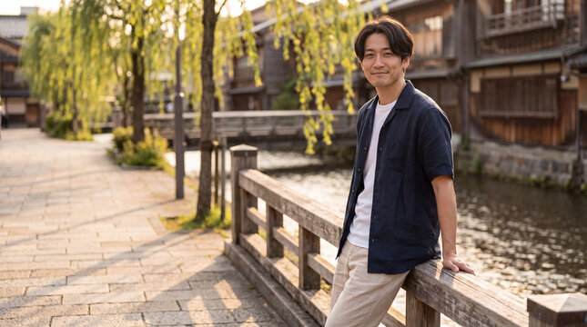 伝統的な町並みの水辺で微笑む落ち着いた男性 ｜ 柔らかな夕光