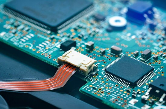 Macro view of electronic motherboard with ribbon cable interface and integrated microchips. Semiconductor manufacturing, artificial intelligence hardware, embedded electronics and modern computing.