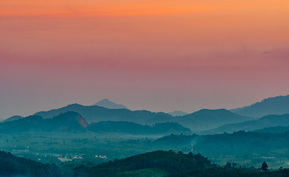 Beautiful layered mountain landscape beneath colorful sunrise sky with soft mist and tropical forest, peaceful panoramic nature scene in Thailand. Warm morning light, scenic travel destination.