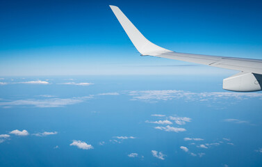 Fototapeta premium Commercial airplane wing seen from passenger window while flying above clouds under clear blue sky. Modern aviation, international flight, travel experience and tourism concept. Global tourism.
