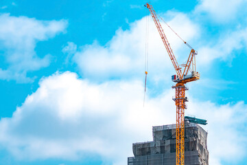 Fototapeta premium Tower crane operating beside a high rise building construction project. Modern civil engineering, infrastructure development, commercial real estate, urban expansion and construction industry concept.