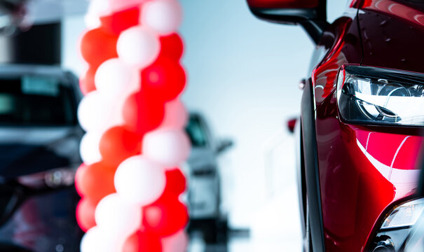 Modern red SUV displayed in car showroom with illuminated LED headlight and promotional balloons, premium automobile dealership interior for vehicle sales, automotive marketing and transportation.