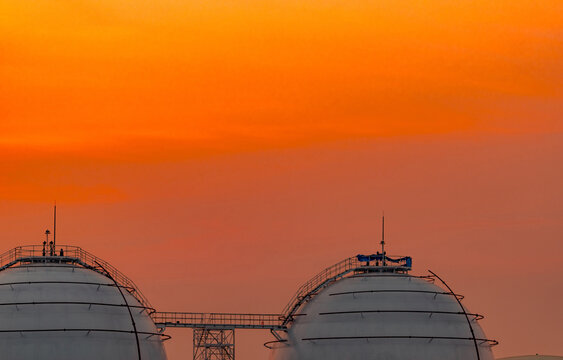 Large spherical LNG storage tanks at a petroleum refinery during orange sunset, industrial natural gas infrastructure supporting global energy supply, storage, transportation and consumption.