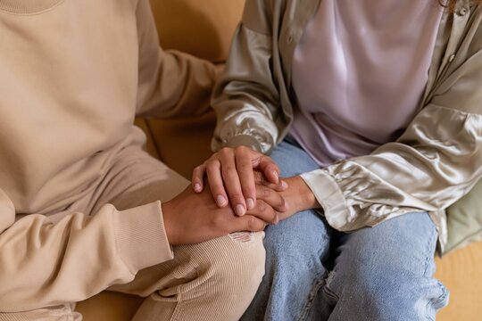 Close up of a couple holding hands in a supportive gesture on a sofa for mental health and relationship counseling themes