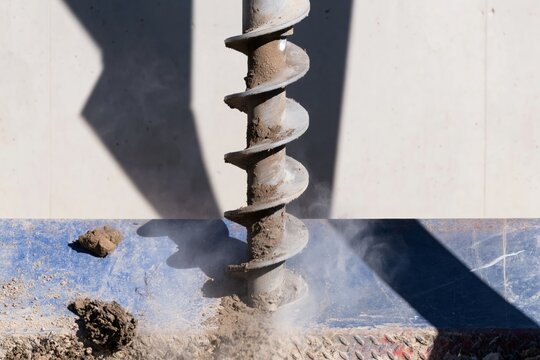 Industrial soil auger bit drilling into the earth with caked mud and dust for construction and geotechnical engineering concepts