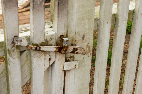 Rustic white picket fence gate with oxidized iron latch in Historic Williamsburg, Virginia.