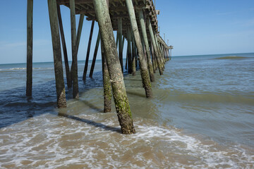 Weathered wood pilings support a pier stretching out into the Atlantic Ocean, taken from the beach, under and to the right side looking out.  © Archival Stone Stock