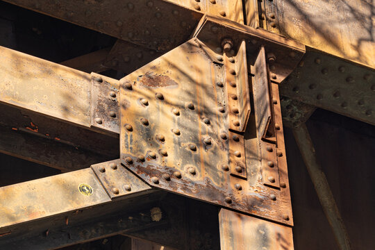 Tree shadows rake across the oxidized iron beams and rivets of a Shockoe Bottom elevated train track in Richmond, Virginia. 
