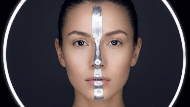 Professional studio beauty portrait of female model with reflective liquid silver face stripe
