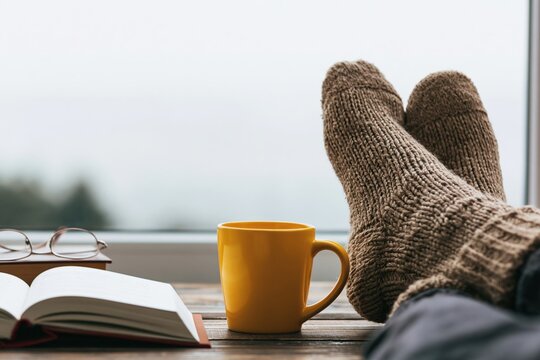 Cozy autumn day with a person relaxing by the window with tea and wool socks book