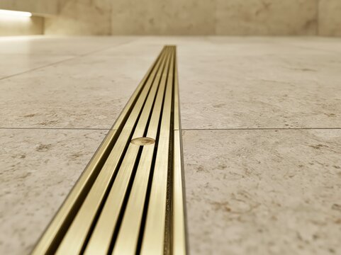 Brushed brass linear shower channel drain in modern spa bathroom with stone tile