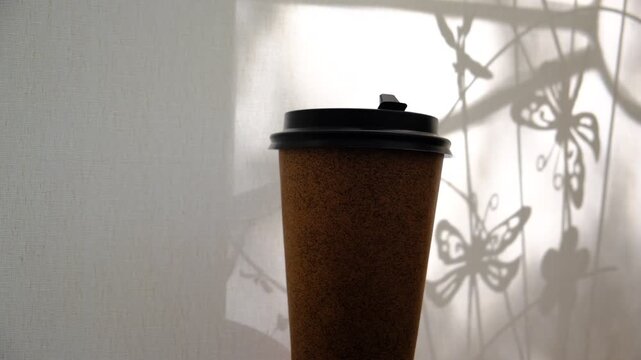 Take away kraft coffee cup on a sunlit window sill in a cozy cafe. A warm morning scene with a rustic kraft paper cup of aromatic coffee. Soft daylight streams through the window, casting gentle shado