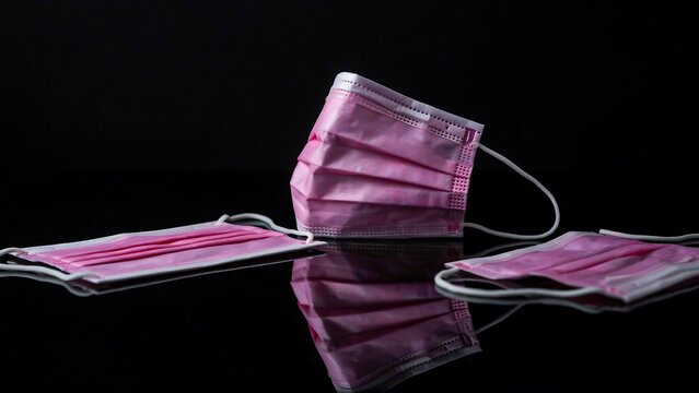 Pink disposable surgical face masks on black reflective surface for healthcare protection