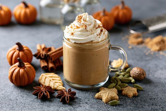 Pumpkin latte with whipped cream and cinnamon spices on a rustic autumn table