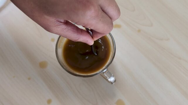 Hand Stirring Hot Coffee with Spoon in Glass Cup