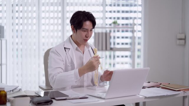 Young Asian doctor examining anatomical spine model while using laptop in modern medical office with city view