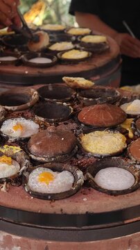 Traditional Vietnamese street food Banh Can cooking in small clay pots on outdoor stove. Quail eggs frying on rice flour pancake batter, authentic Asian culinary culture and local market gastronomy.