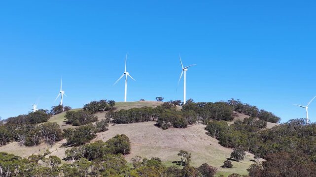 Wind Turbines Spinning on Rural Hillside Under Clear Blue Sky