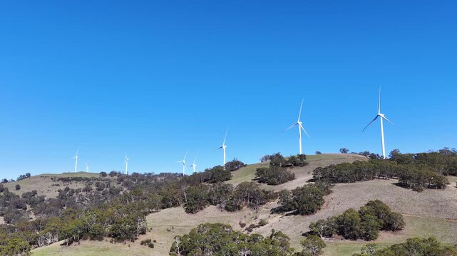Wind Turbines Rotating on Green Hills Under Clear Blue Sky