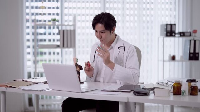 Young Asian doctor examining prescription medicine bottles while consulting laptop in modern medical office