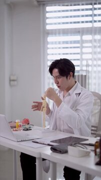 Young Asian male doctor examining skeletal model anatomy at modern medical office desk with laptop