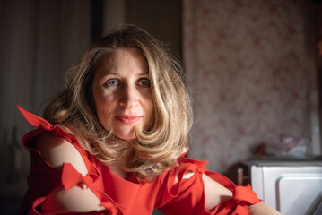 Thoughtful caucasian woman in red dress sitting at a bar or cafe at night, holding a smartphone, with a blurred glass of wine or cocktail in the foreground with dim lighting. © shymar27