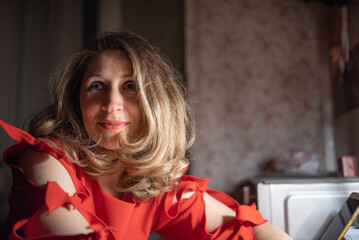 Thoughtful caucasian woman in red dress sitting at a bar or cafe at night, holding a smartphone, with a blurred glass of wine or cocktail in the foreground with dim lighting. © shymar27