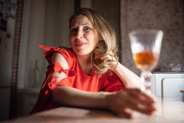 Thoughtful caucasian woman in red dress sitting at a bar or cafe at night, holding a smartphone, with a blurred glass of wine or cocktail in the foreground with dim lighting. © shymar27