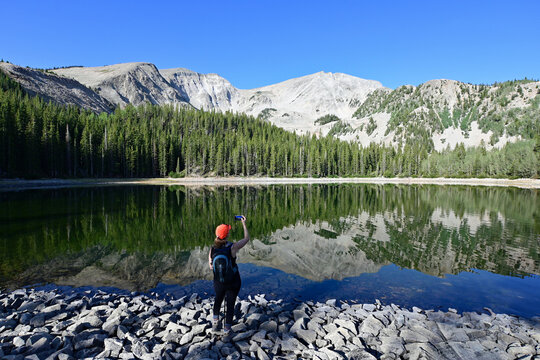 Woman explores shore of second Thomas Lake in Maroon Bells-Snowmass Wilderness in White River National Forest on calm clear summer morning.