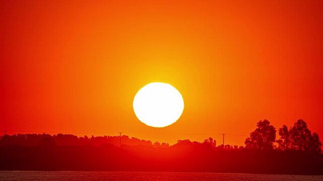 View of a vibrant red sunset dipping below the horizon with silhouettes of trees in Riga, Latvia.