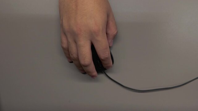 Overhead close-up of a hand naturally using a computer mouse, performing clicks and cursor movements in a modern office workspace.