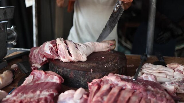 Butcher chopping raw pork leg with cleaver and hammer on wooden block at Vinh Hai market in Nha Trang, Vietnam. Close up view of fresh meat preparation at traditional Asian street market counter.