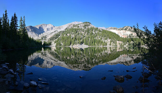 Panorama of Mount Sopris reflected in calm water of Thomas Lake in Maroon Bells-Snowmass Wilderness near Carbondale, Colorado on sunny summer morning.