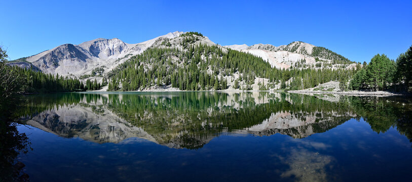 Panorama of Mount Sopris reflected in calm water of Thomas Lake in Maroon Bells-Snowmass Wilderness near Carbondale, Colorado on sunny summer morning.