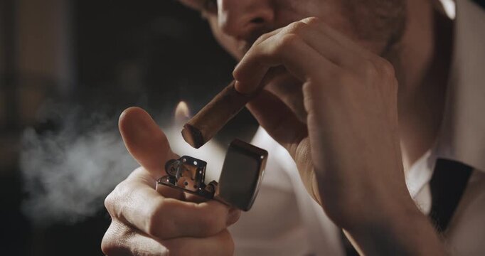 Close-up of a man lighting a cigar and smoking it with apparent pleasure in warm dramatic light.