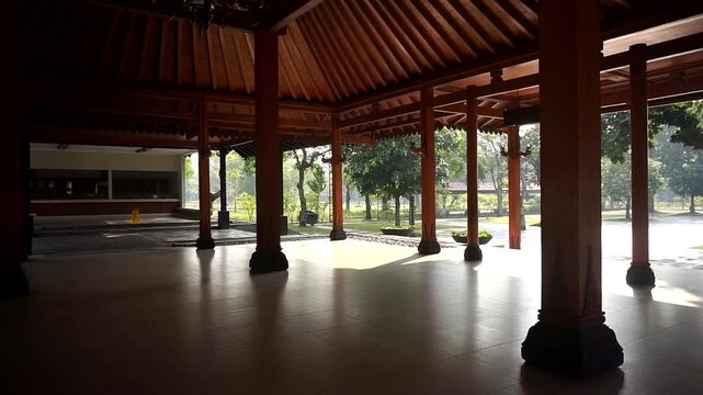 Interior of a traditional Javanese wooden building featuring sturdy support pillars and a lush courtyard atmosphere.
