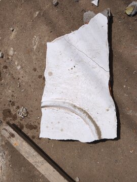 Broken piece of white plaster molding lying on dirty ground outdoors