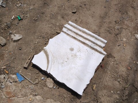 Broken piece of white plaster architectural molding on dirt ground