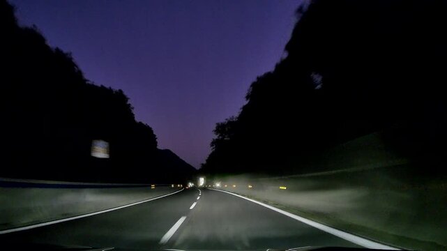 Forward dashcam view from car driving on expressway with streetlights illuminating dark landscape at night