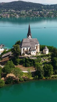 Vertical Drone Shot of Parish Catholic Church in Maria Worth Village. Landmark Above Worthersee Lake on Sunny Summer Day